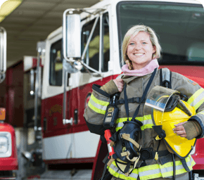 firefighter in gear smiling and standing in front of a firetruck.png